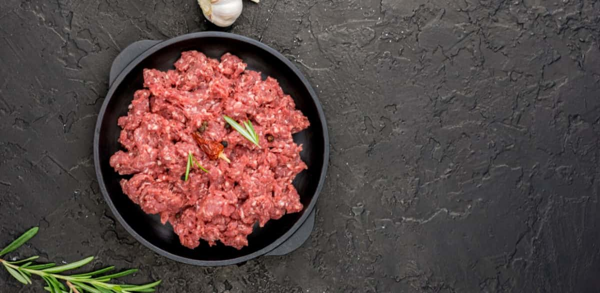 Ground beef with herbs in a skillet on a dark textured surface