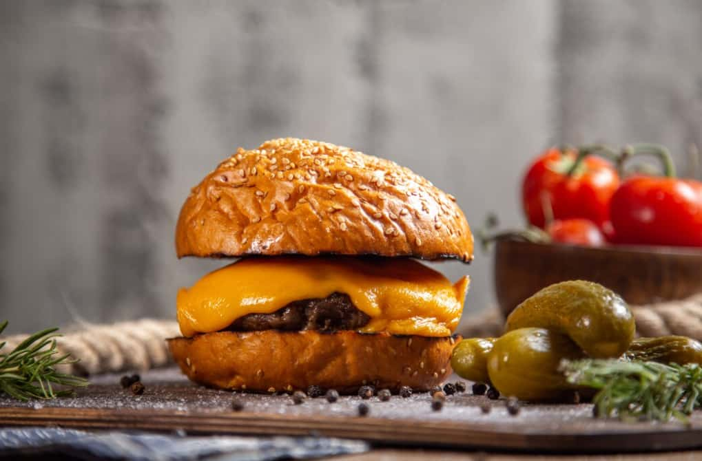 A juicy cheeseburger with tomatoes and pickles on the side