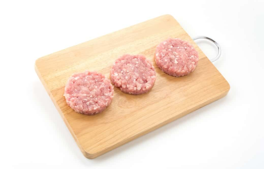 Three raw burger patties on a wooden cutting board