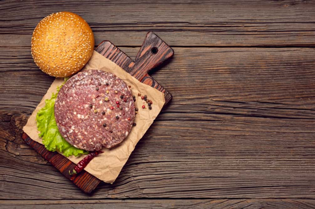 An uncooked burger patty with spices on parchment pape