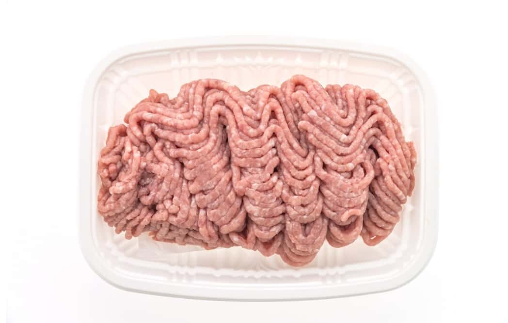 Striped ground beef in a white plastic tray on a white background