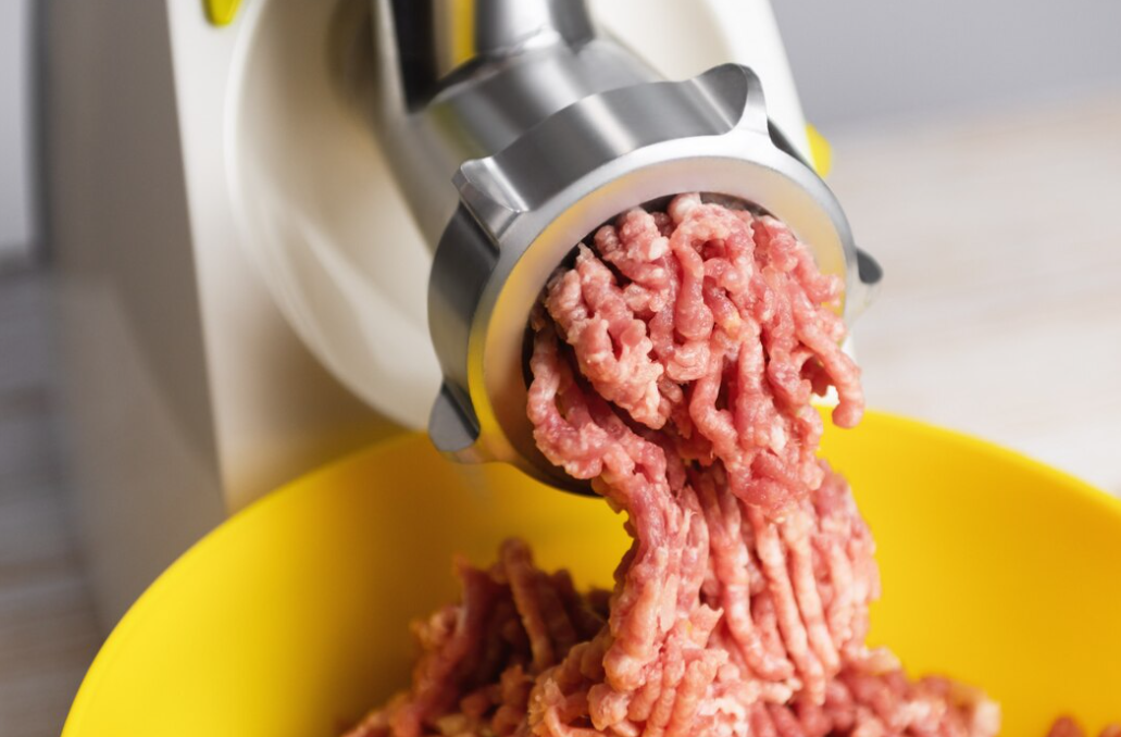 Ground beef extruding from a grinder into a yellow bowl