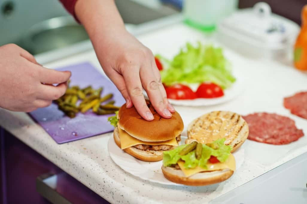 Hands assembling a cheeseburger with various toppings