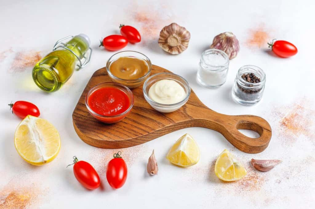 A variety of condiments and fresh tomatoes on a kitchen counter